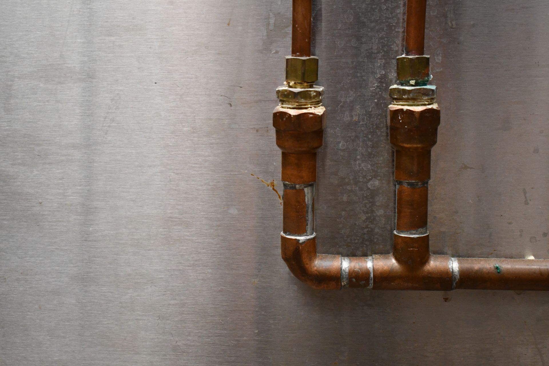 Copper pipes with fittings against a metal wall. Copper pipes with fittings against a metal wall.