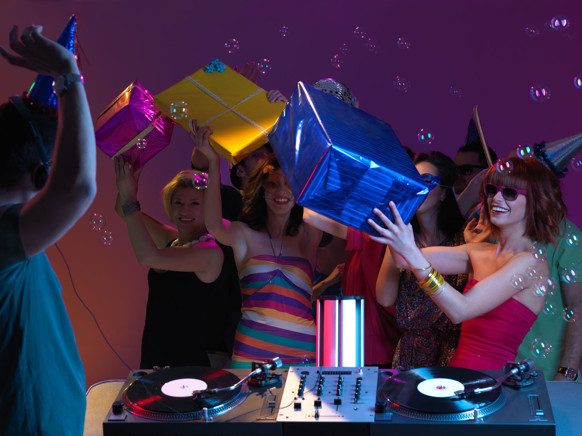 Crowd dancing around a DJ booth with colorful mirrored cubes under purple lights
