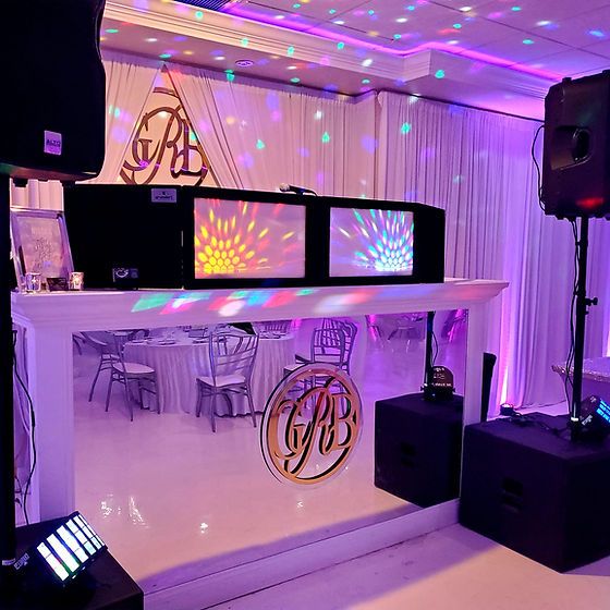 DJ booth with colorful lights and speakers in a dark room with a draped backdrop