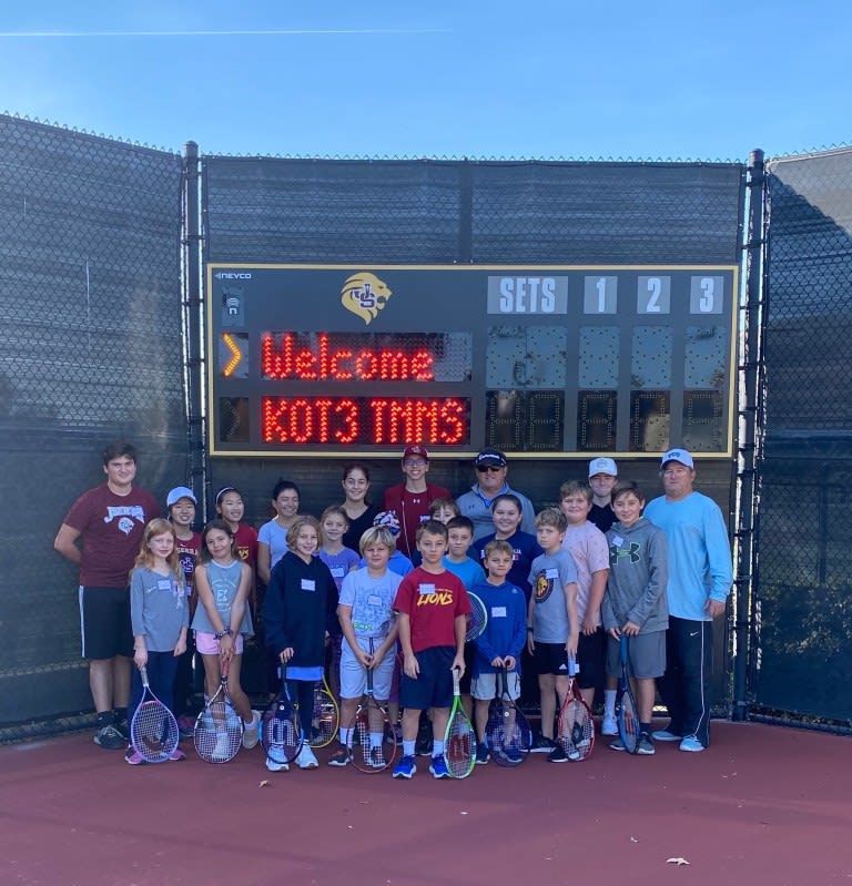 A group of people standing in front of a scoreboard that says welcome kot3 tennis