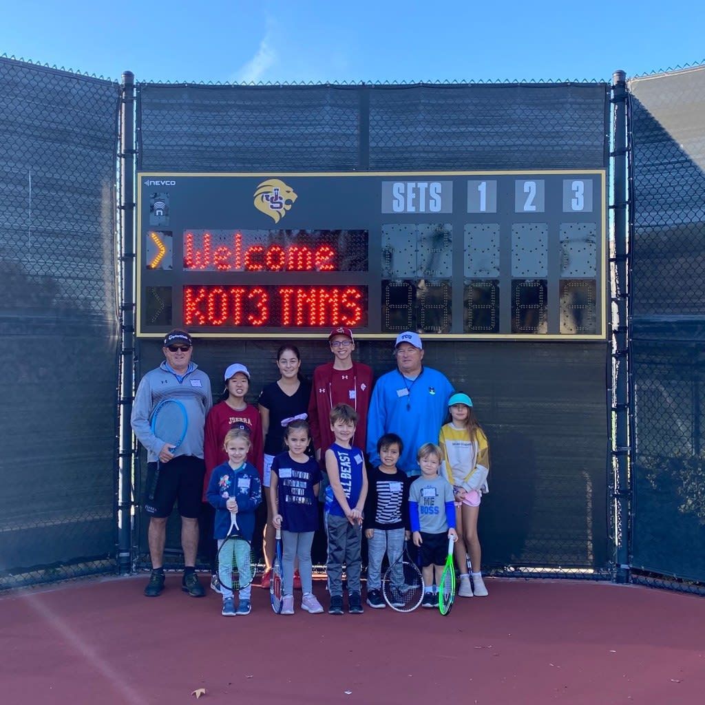 A group of people standing in front of a scoreboard that says welcome kot3 thns