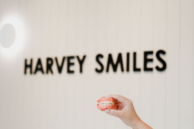A Business Card For Harvey Smiles Is Sitting On A Wooden Table — Harvey Smiles Denture Clinic In Burleigh Heads, QLD