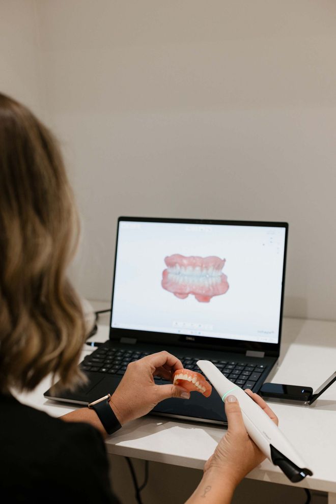 A Woman Is Sitting At A Desk In Front Of A Laptop Computer — Harvey Smiles Denture Clinic In Burleigh Heads, QLD