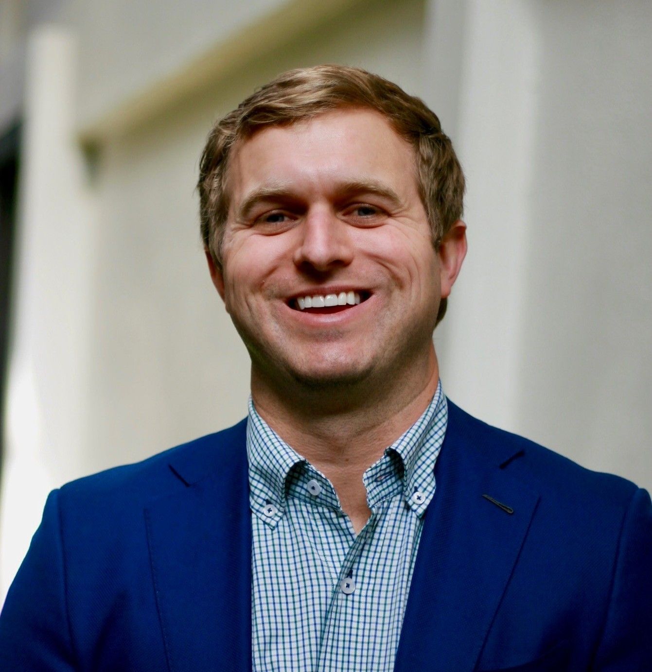Man in a blue blazer and patterned shirt smiles outdoors.