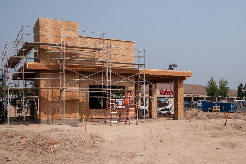 Construction site of a building, scaffolding around a wooden frame, dry dirt.