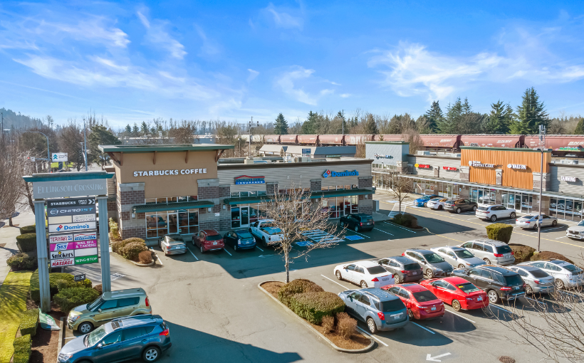 Shopping center exterior with cars parked out front, under a sunny, blue sky.