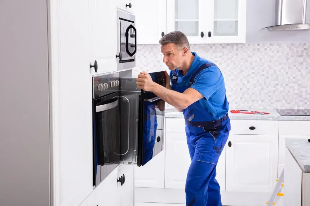 Technician in Blue Workwear Installing a Built-in Oven in a Bright — Eurocoast Appliance Service In Tuggerah, NSW