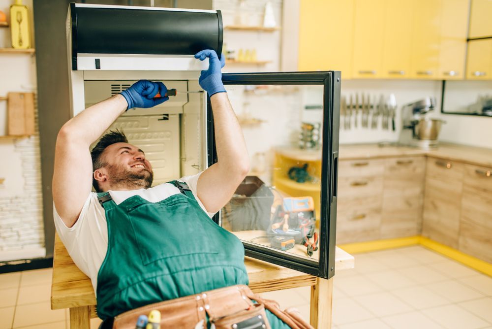 Person Repairs a Small Refrigerator on a Wooden Table — Eurocoast Appliance Service In Morisset, NSW