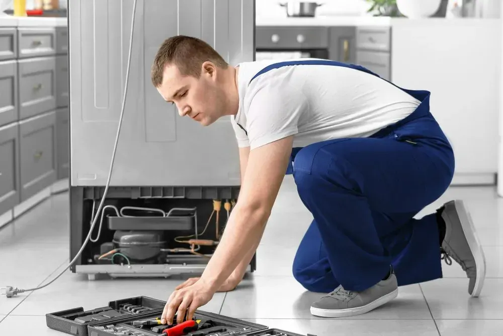 Person in Blue Overalls Kneels on a Kitchen Floor — Eurocoast Appliance Service In Tuggerah, NSW