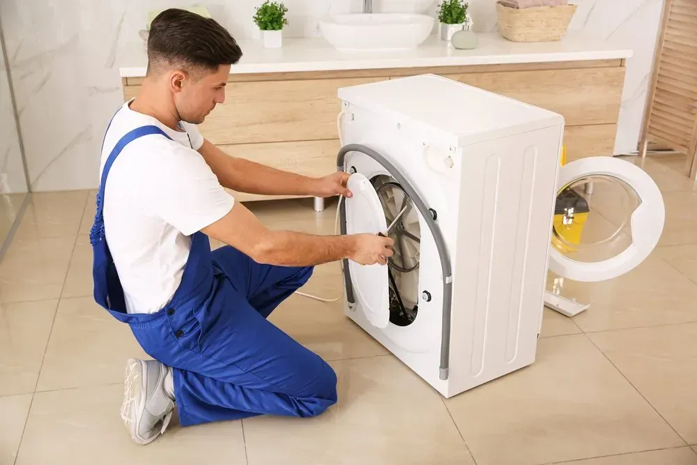 Technician in Blue Overalls Kneels on a Tile Floor — Eurocoast Appliance Service In Tuggerah, NSW