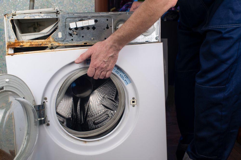 Person in Blue Work Pants Repairs a White Washing Machine— Eurocoast Appliance Service In Tuggerah, NSW