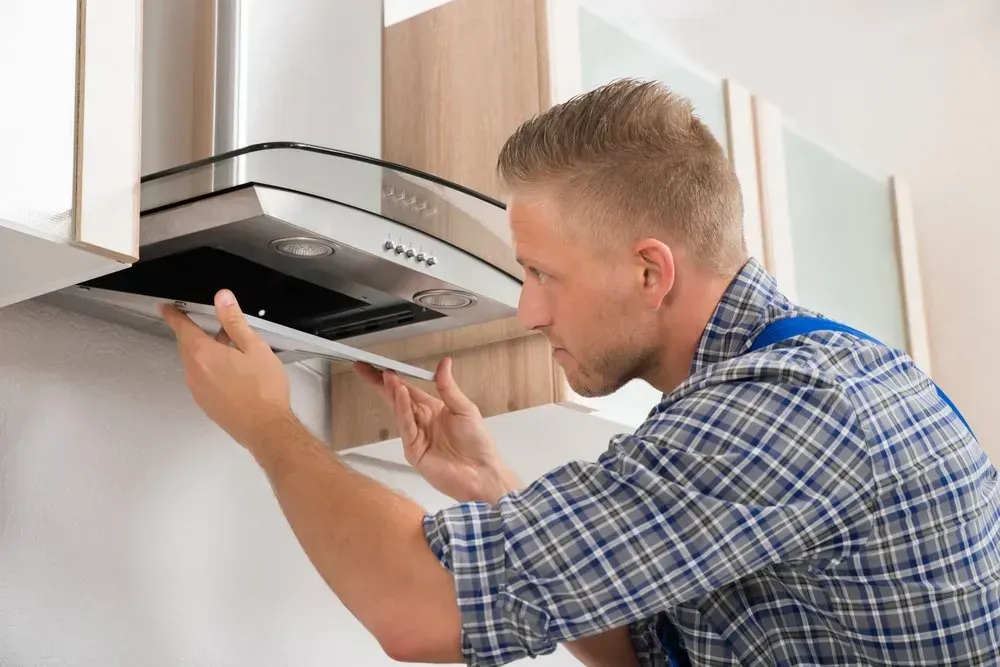 A Person Repairs a Stainless Steel Range Hood in a Kitchen — Eurocoast Appliance Service In Woy Woy, NSW