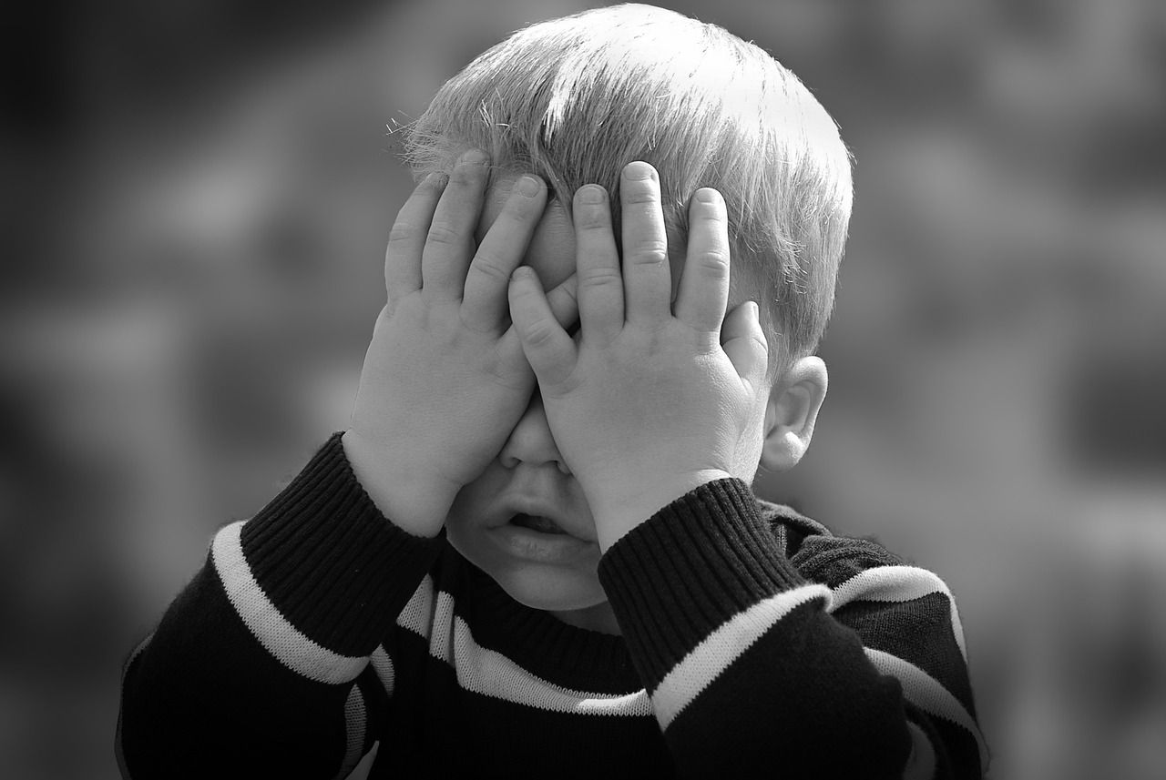 Little boy covering his eyes with his hands in black and white