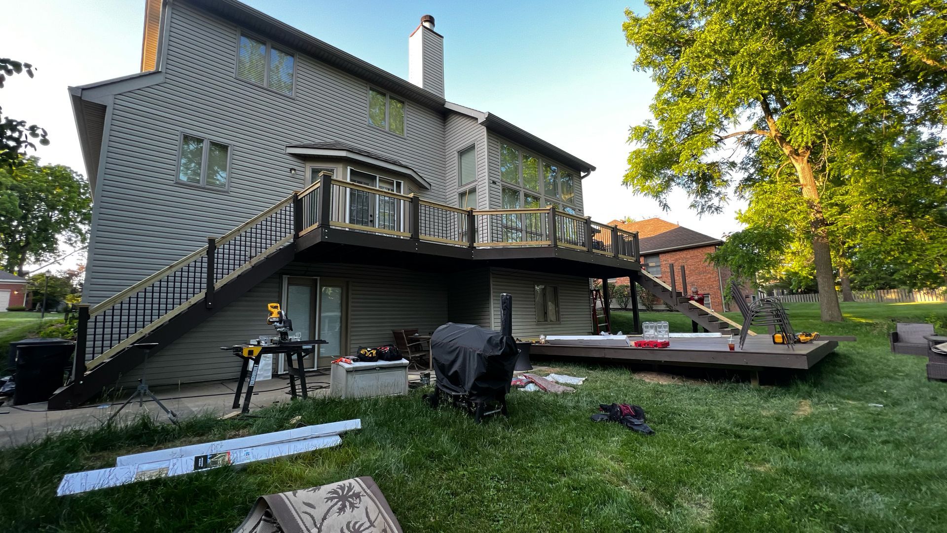Two-story house with a wooden deck being built on a grassy backyard.