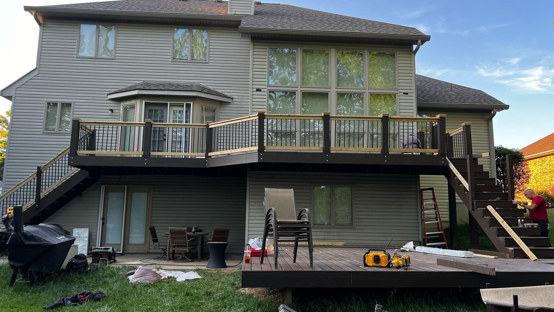 Two-story house with a wooden deck being built; dark brown railings, light siding.