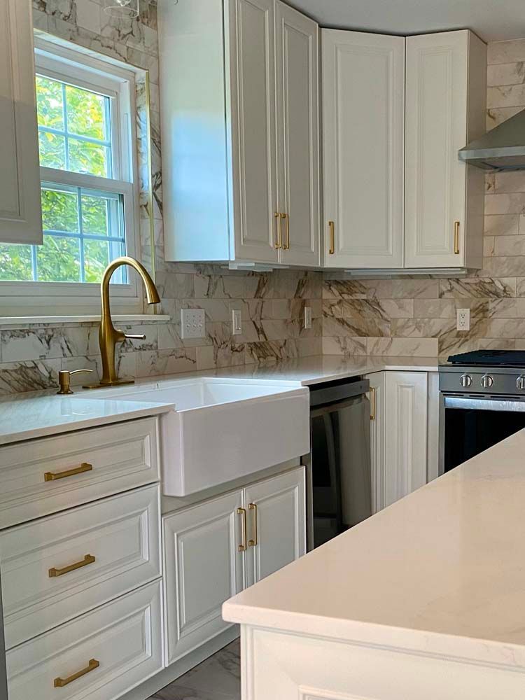 White kitchen with gold fixtures, marble backsplash, and stainless steel appliances.