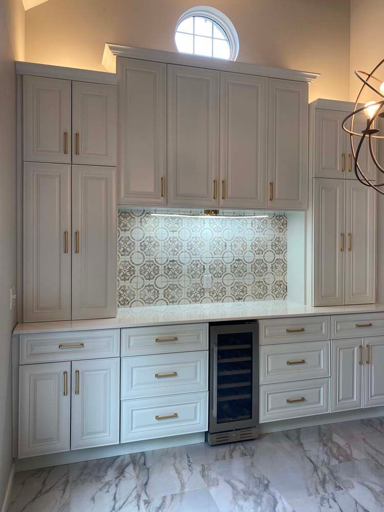 White kitchen cabinets with gold hardware and a patterned backsplash above a wine cooler.