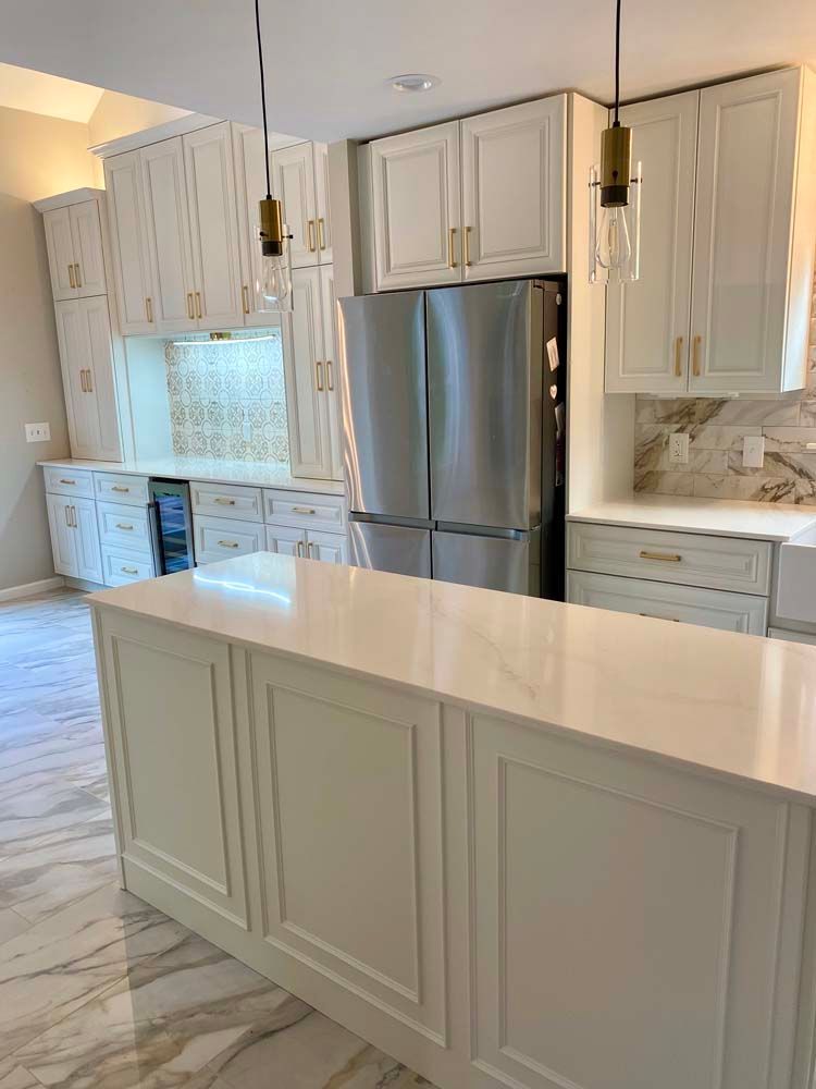 White kitchen with island, stainless steel refrigerator, white cabinets, gold hardware, and marble flooring.
