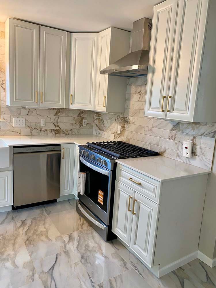 White kitchen with cabinets, stainless steel appliances, marble backsplash, and gold hardware.