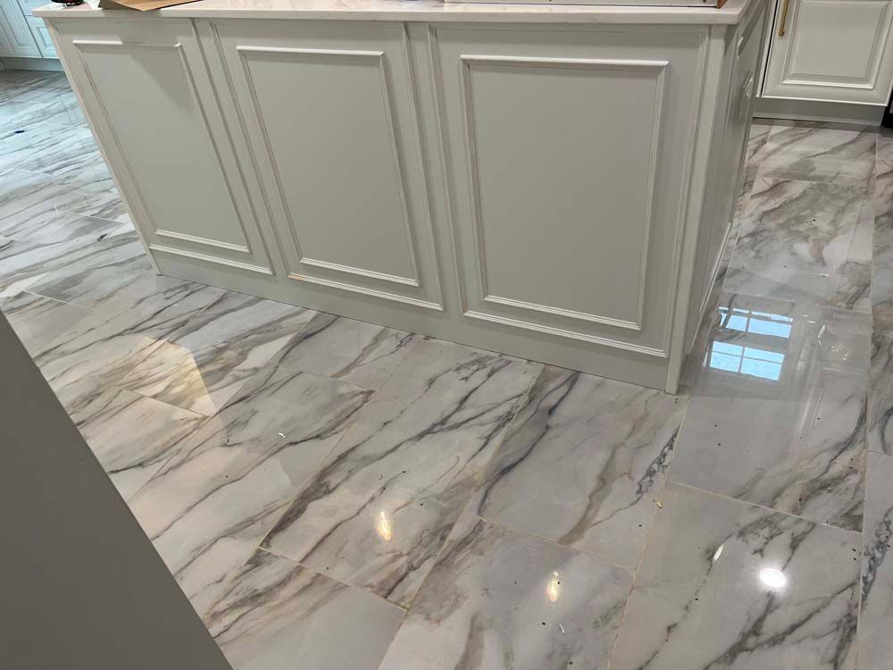 White kitchen island with paneled details on glossy marble-patterned flooring.