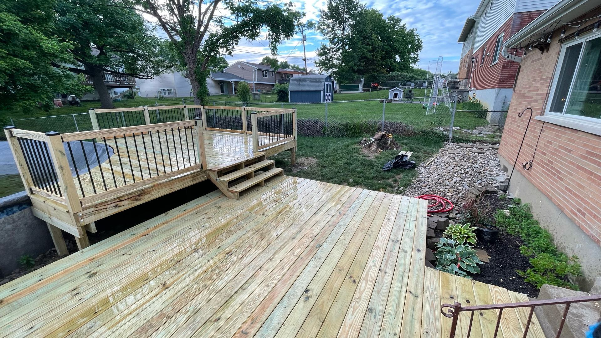 New wooden deck with stairs in a backyard next to a brick house.