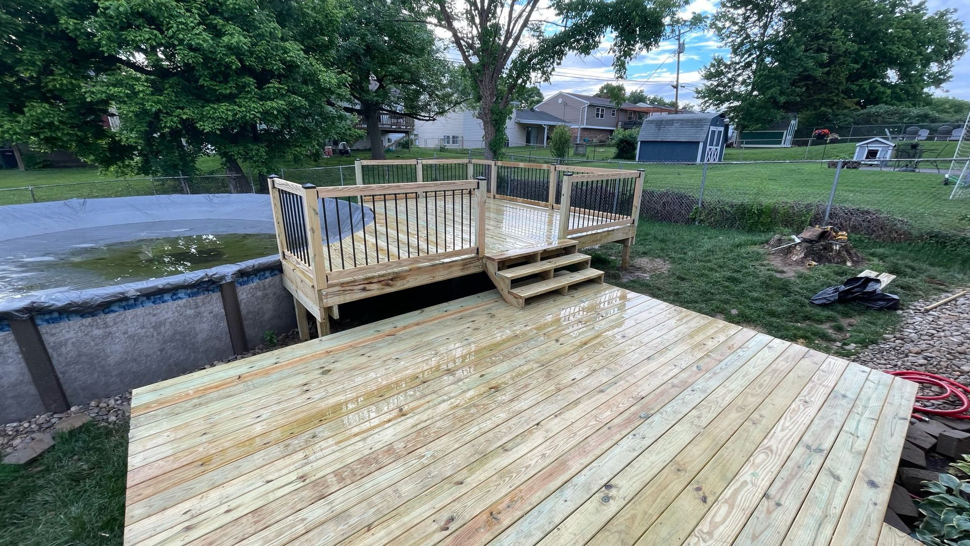 Newly built wooden deck with steps, connected to a raised pool and overlooking a green lawn.