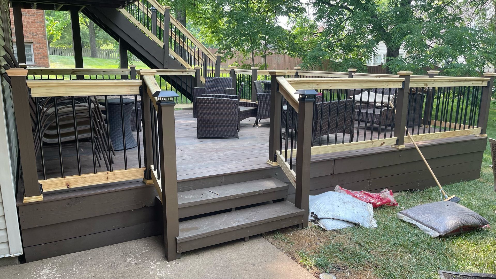 Brown deck with stairs, railing, and outdoor furniture. Bags and pillows on the grass.