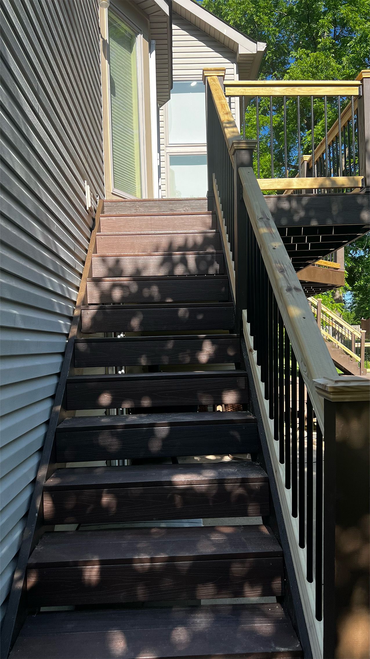 Outdoor wooden staircase leading up to a deck, attached to a house with gray siding.