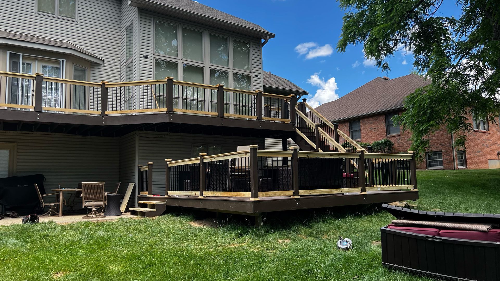 Multi-level wooden deck attached to a light-colored house, with grass in the foreground and a blue sky overhead.