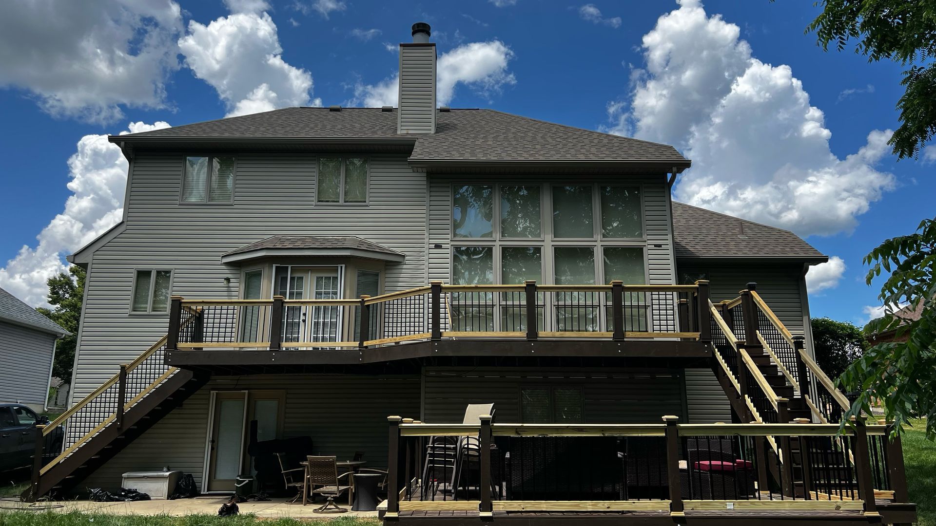 Two-story house with brown deck and stairs. Cloudy blue sky in the background.