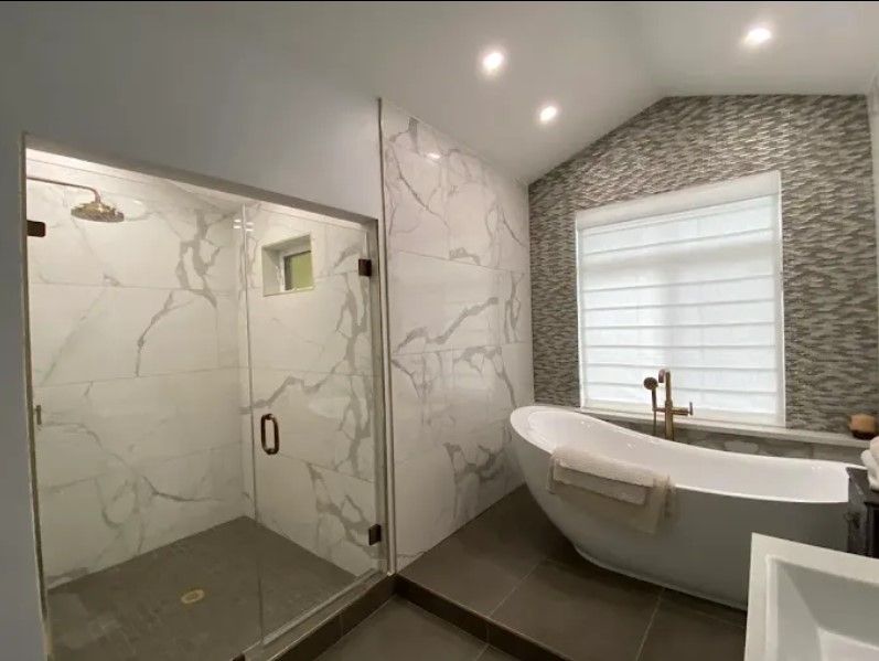 Modern bathroom with a glass-enclosed shower, freestanding tub, and marble and mosaic tile walls.