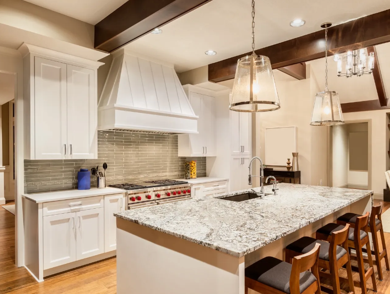 White kitchen with island, range, and hood; wood beams and pendant lights.