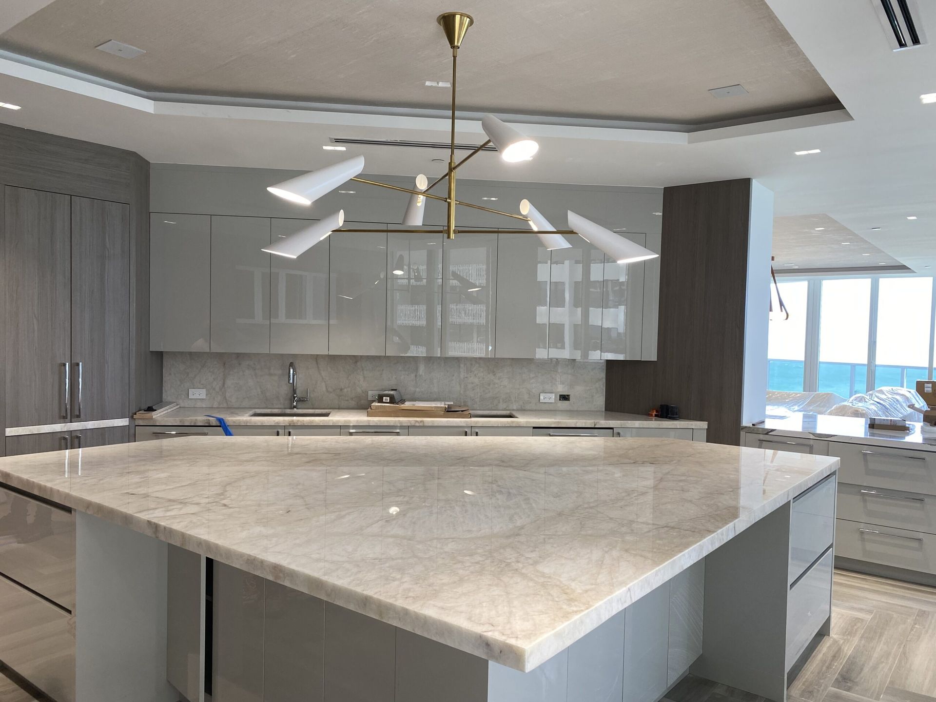 Modern kitchen with large island, glossy grey cabinets, and a decorative light fixture.