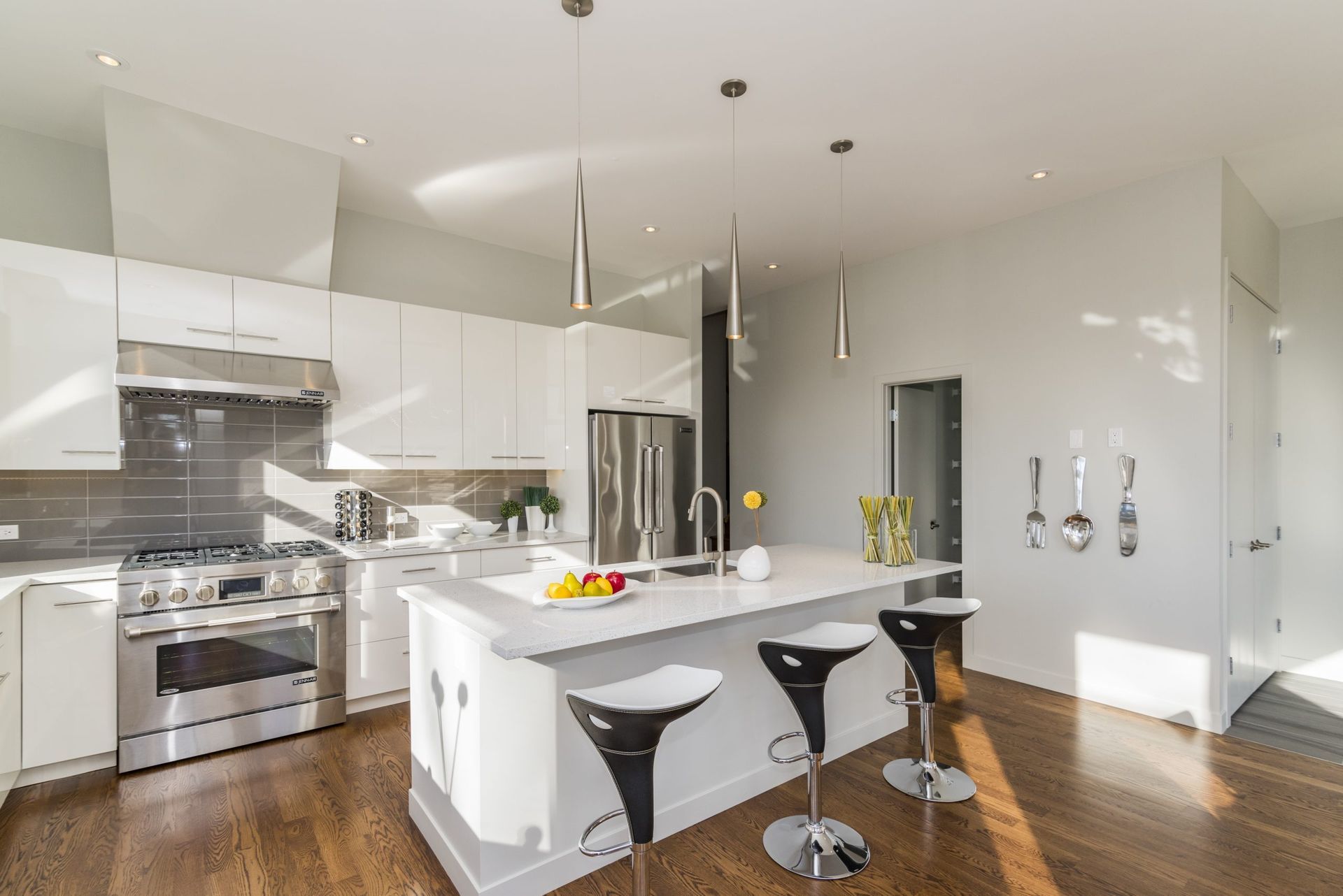 Modern white kitchen with island, stainless steel appliances, dark wood floors, and bar stools.