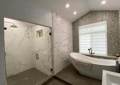 Modern bathroom with marble shower, freestanding tub, mosaic wall, and window with blinds.