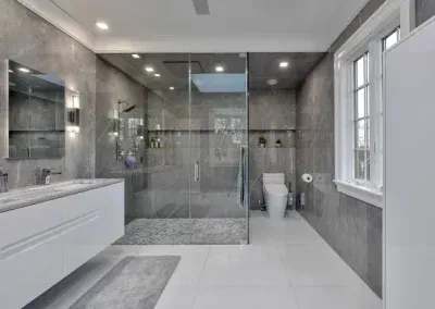 Modern bathroom with gray tiled walls, glass shower, white vanity, and toilet.