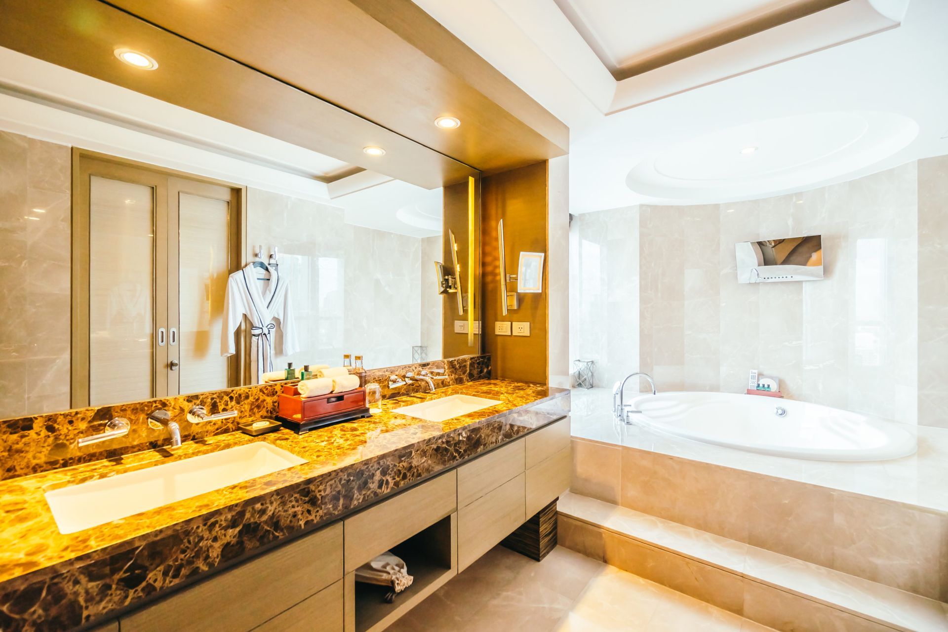Bathroom with marble countertops, sinks, and a large mirror. A bathtub is in the corner.