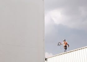 Worker on a rooftop holding a cable, next to a large white structure against a cloudy sky.