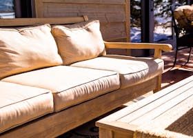 Wooden outdoor sofa with cream cushions on a sunny patio.