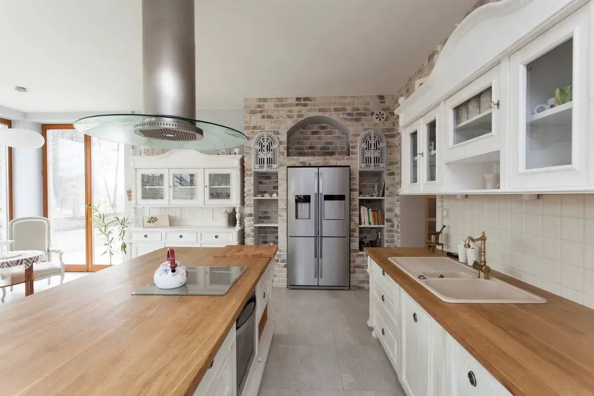 Spacious kitchen with wood counters, white cabinets, stainless steel fridge, and a brick accent wall.