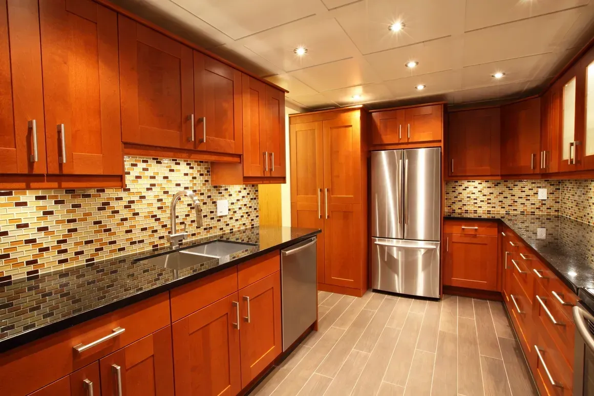 Kitchen with dark wood cabinets, stainless steel appliances, mosaic tile backsplash, and dark countertops.