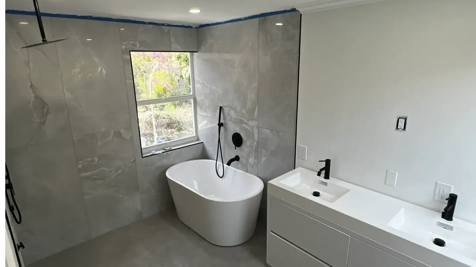 Modern bathroom with gray tiled walls, a white freestanding tub, and a white double-sink vanity.