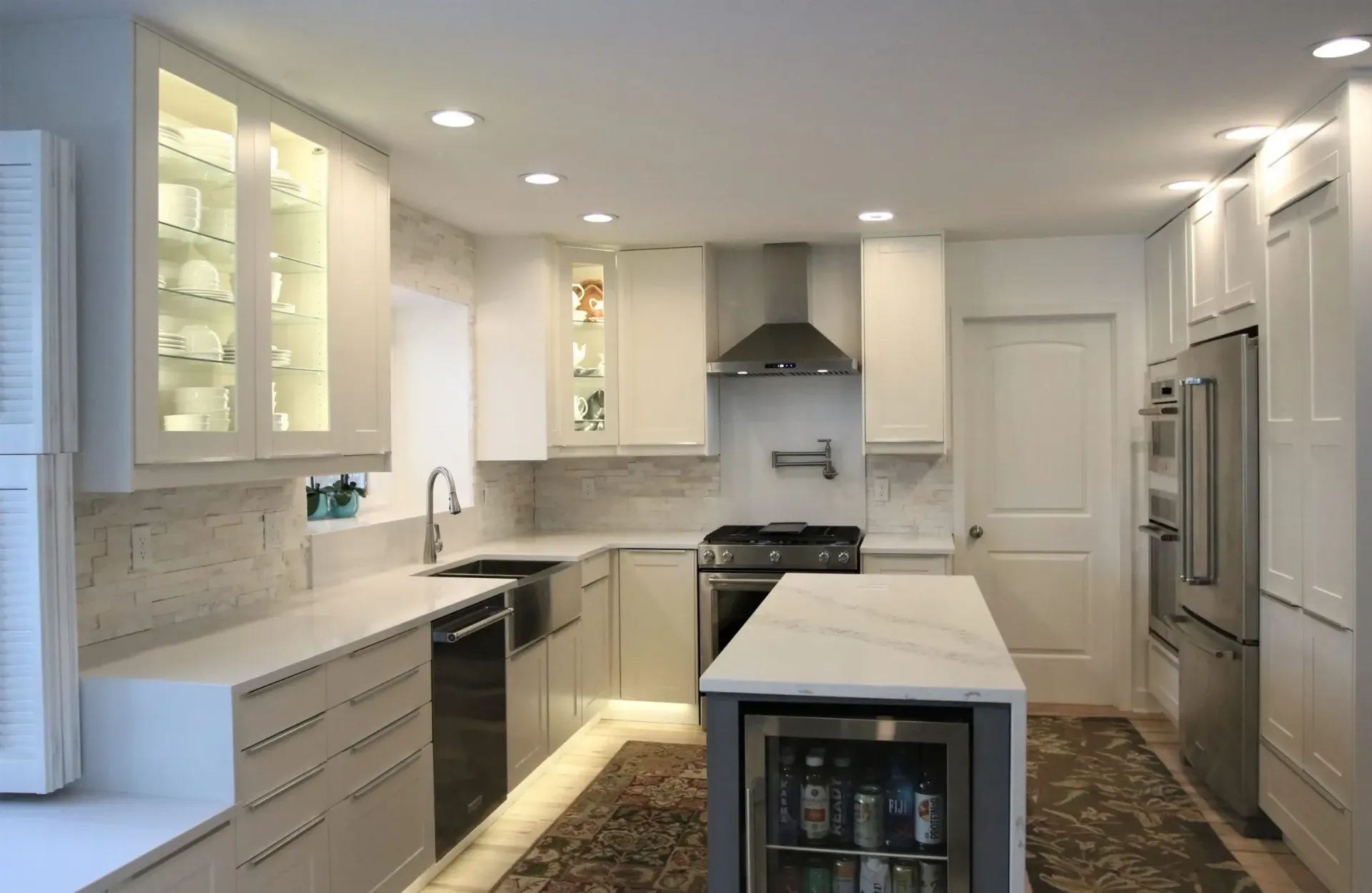 Modern white kitchen with island, stainless steel appliances, and built-in wine fridge.