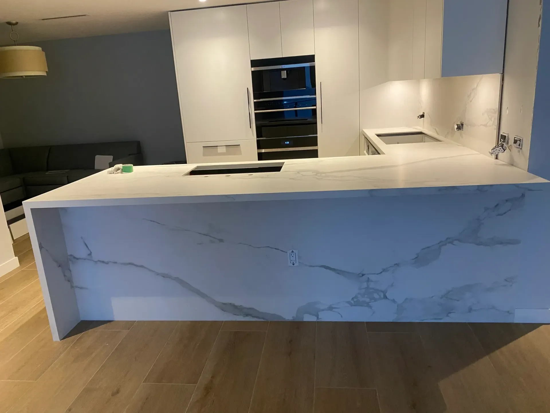 Modern kitchen with white countertops and cabinets, wooden floors, and a built-in oven.