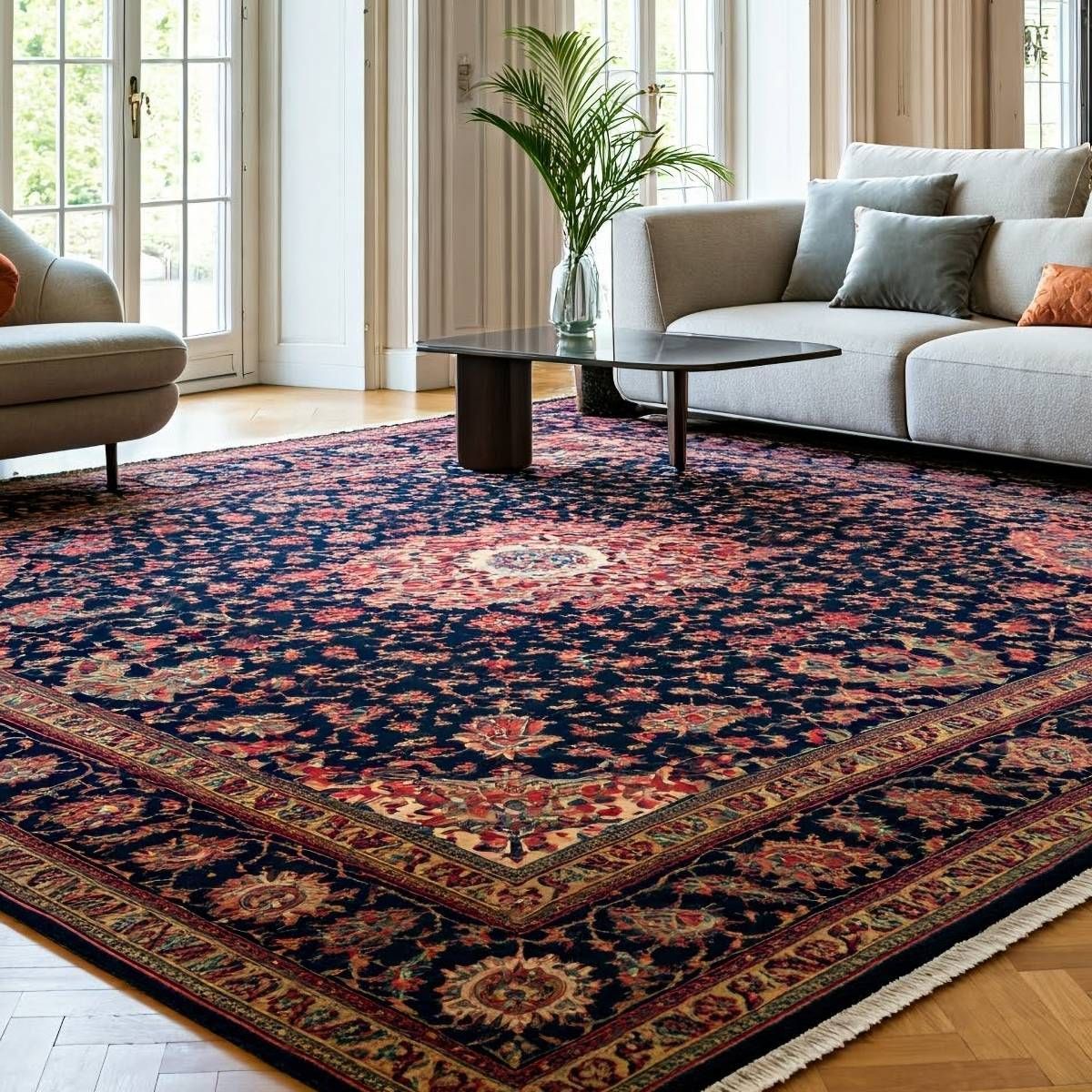 Living room with a large navy, red, and beige patterned rug. Beige sofa and chairs, glass table, and large windows.