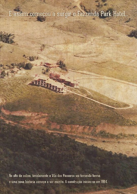 Vista aérea de um chalé em um parque rural, cercado por campos castanhos e floresta escura, com texto sobreposto.
