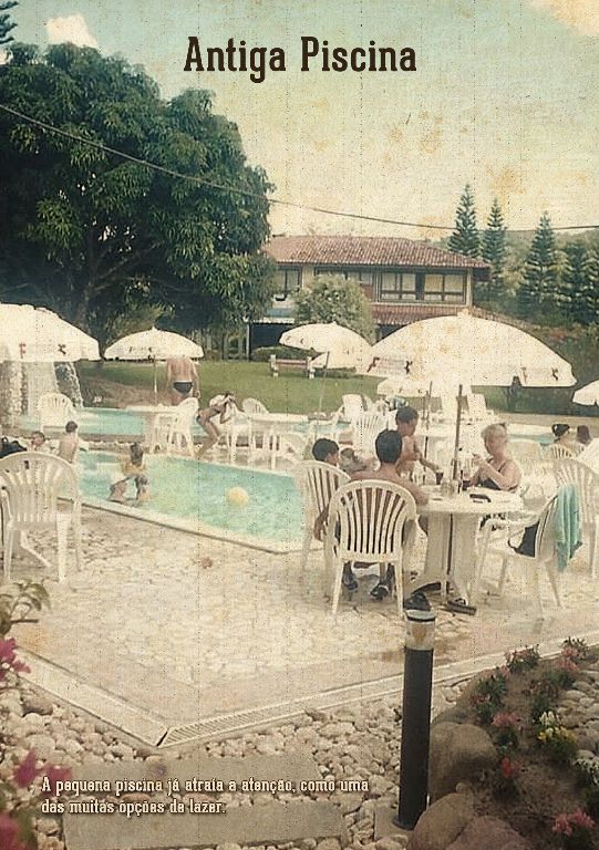 Antiga piscina vintage com pessoas sentadas em mesas ao lado de uma piscina externa turquesa sob guarda-sóis.