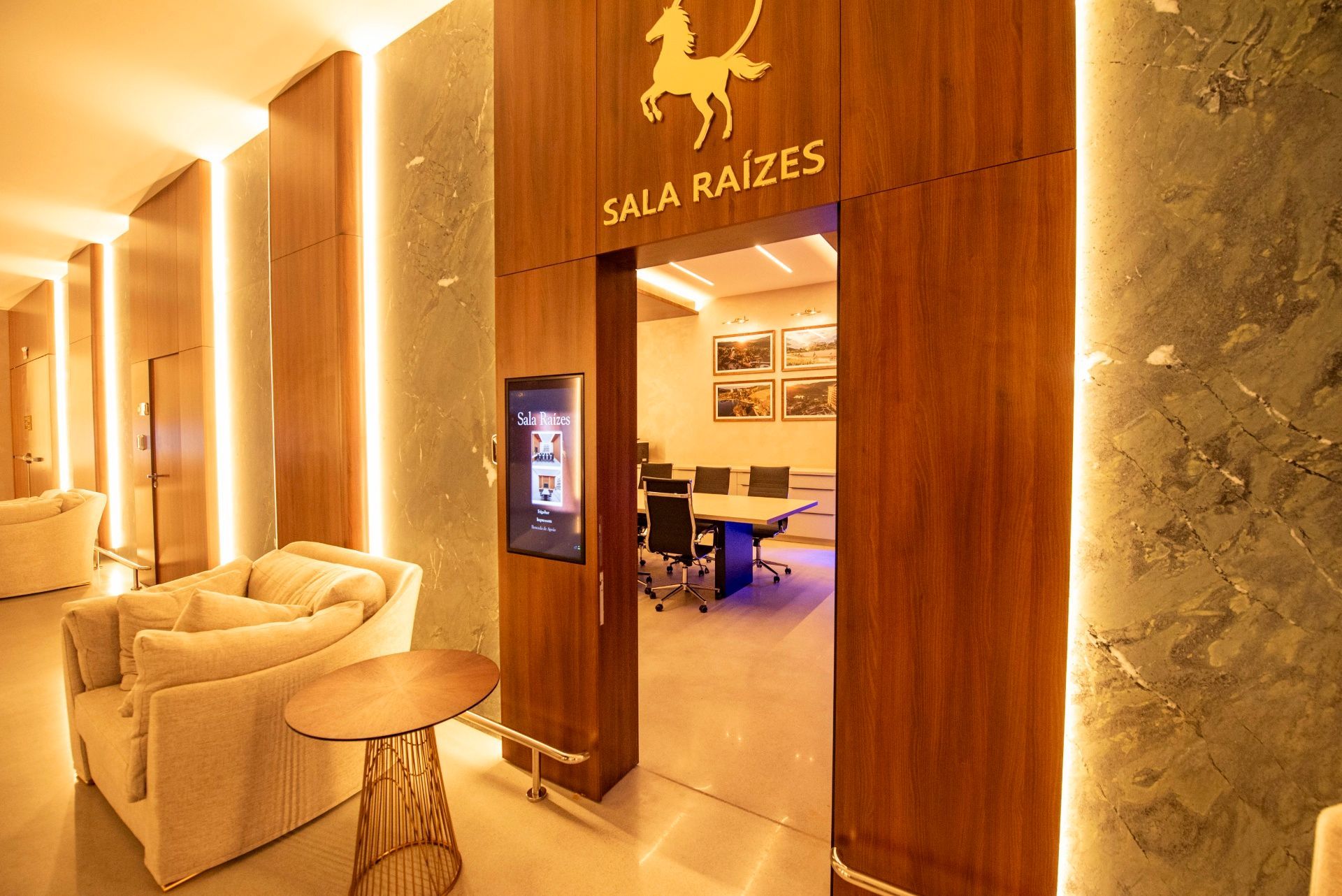 Entrada do spa com iluminação aconchegante, cadeiras cor creme, painéis de madeira e uma placa com os dizeres “SALA RAEZ”.