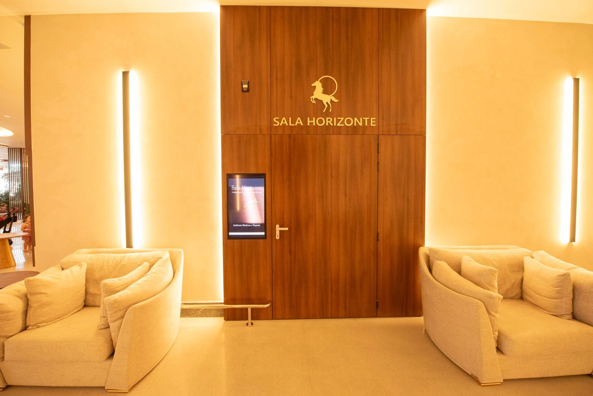 Hall de entrada elegante do hotel com sofás cor creme e uma porta de madeira com a inscrição “Sala Horizon”.