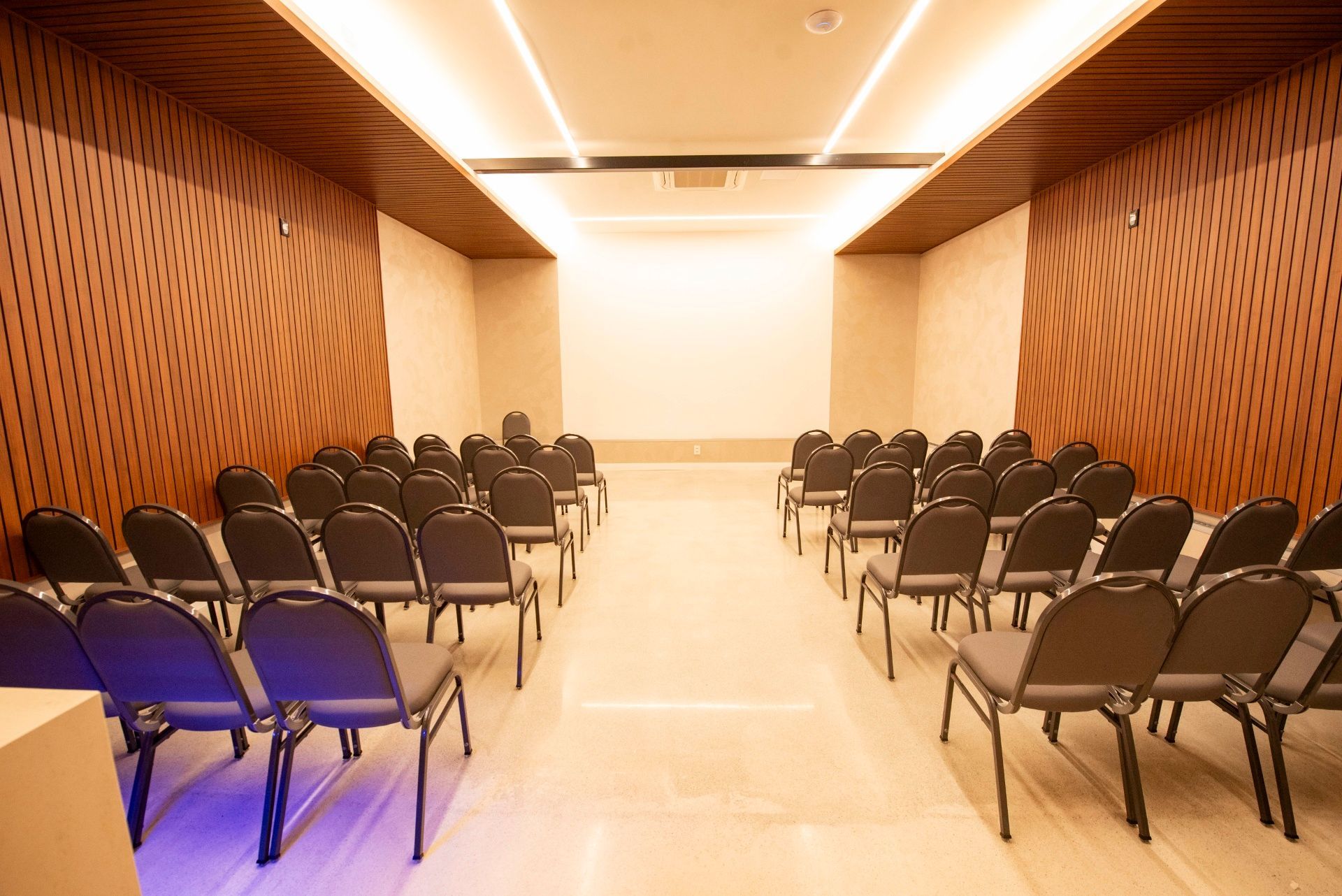 Sala de conferências moderna e vazia, com fileiras de cadeiras pretas e paredes revestidas de madeira em tons quentes.